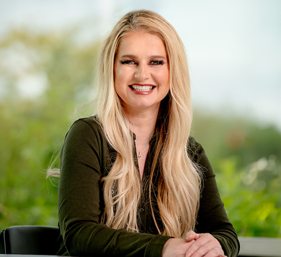 Dr. Robin Pickering with long blonde hair sitting with hands folded, greenery background